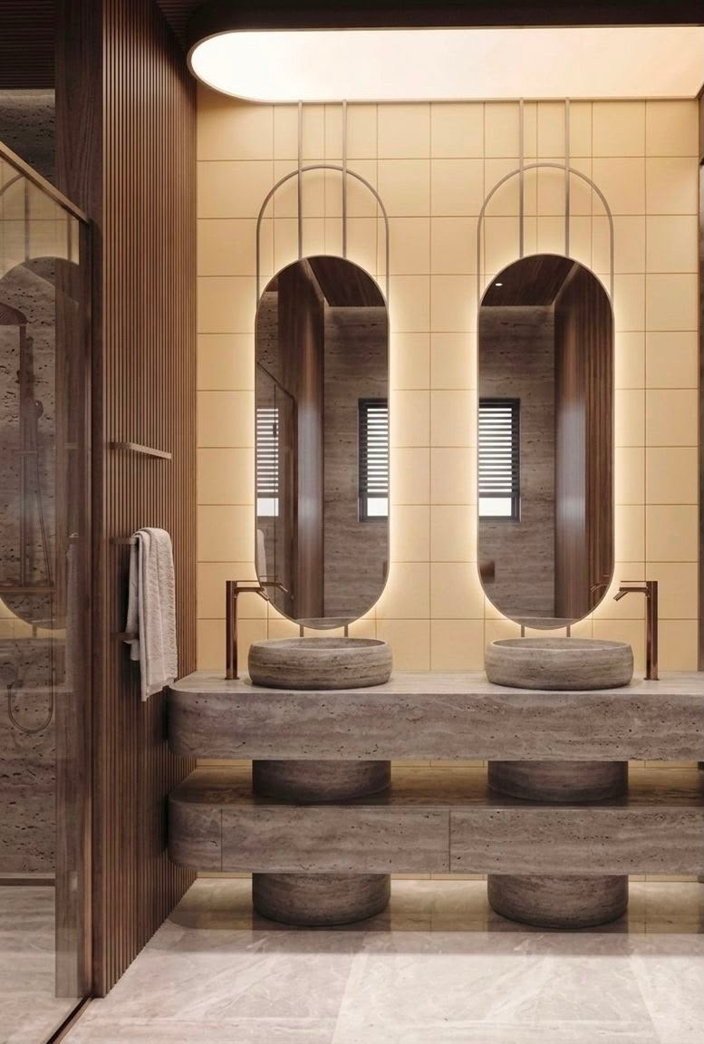 Alabaster luxury residential bathroom in Dubai with twin oval mirrors, stone basins, timber wall panels and backlit feature wall